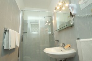 A modern bathroom with a glass shower enclosure, a white sink, and a hairdryer mounted on the wall. - Hotel San Vitale (Medicina)