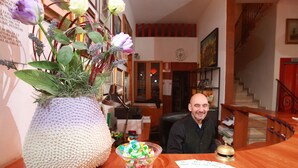 A wooden reception desk with a large textured vase of flowers, a glass bowl of colorful candies, and a bell. - Hotel San Vitale (Medicina)