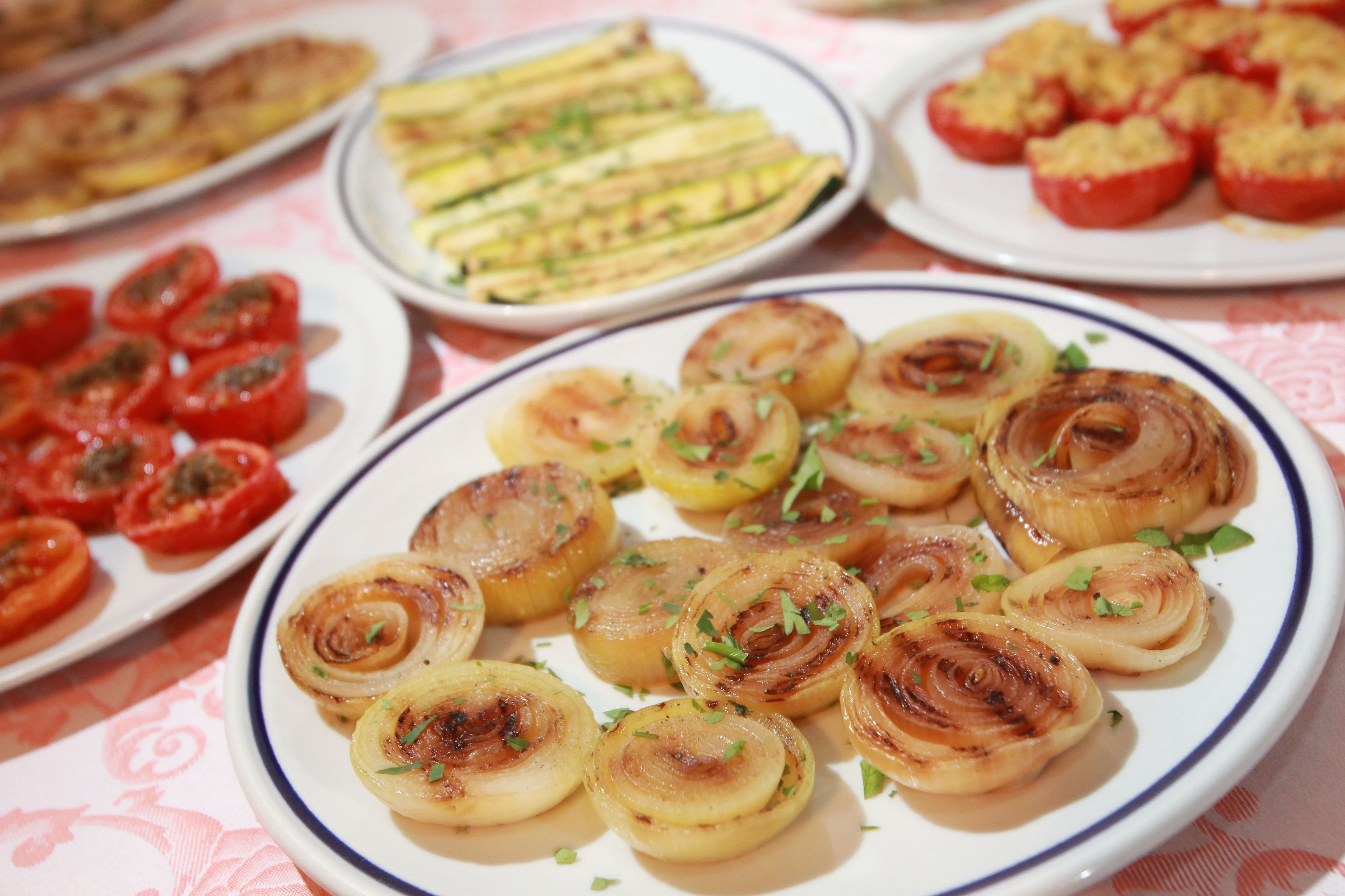 A table with various dishes including grilled onions and stuffed tomatoes.