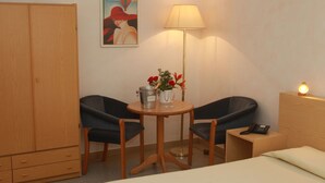 A hotel room with a bed, a wooden wardrobe, two black chairs, a small round table with a lamp, a vase with flowers, and a painting on the wall. - Hotel San Vitale (Medicina)