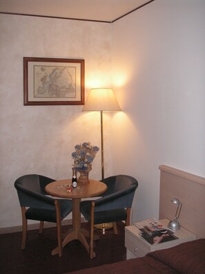 A small room with a round table, two chairs, a floor lamp, a framed map on the wall, and a nightstand with a lamp and magazines. - Hotel San Vitale (Medicina)