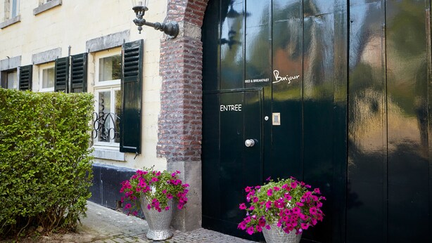 Una puerta negra con letreros que dicen "ENTREE" y "Bed & Breakfast", un arco de ladrillo y dos macetas con flores rosas.