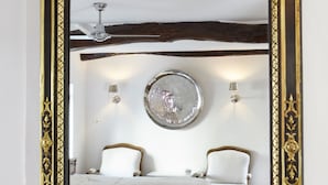 Un dormitorio con cama, dos sillas, un espejo redondo y una lámpara de araña.