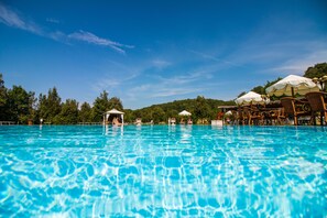 A clear blue pool with lounge chairs and umbrellas, surrounded by trees and a hill in the background. - Relais Santa Margherita (Capolona)