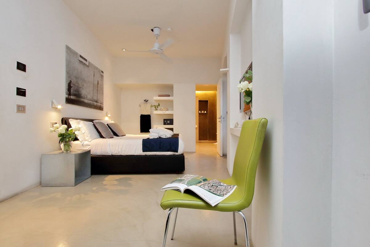 A modern bedroom with a bed, bedside tables, a green chair, and a ceiling fan.