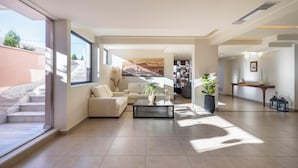 A spacious living room with a large window, a sofa, a coffee table, and a bookshelf. - Harmony Hotel Nafplio (Nafplio)