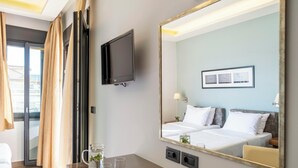 A hotel room with a bed, a TV, a mirror, and a desk with glasses and a vase. - Harmony Hotel Nafplio (Nafplio)