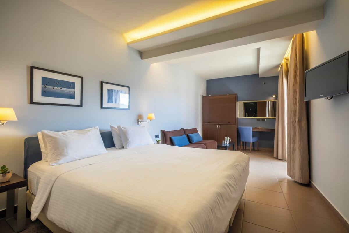 Una habitación de hotel con una cama grande, un escritorio, una silla, un televisor y una kitchenette.
