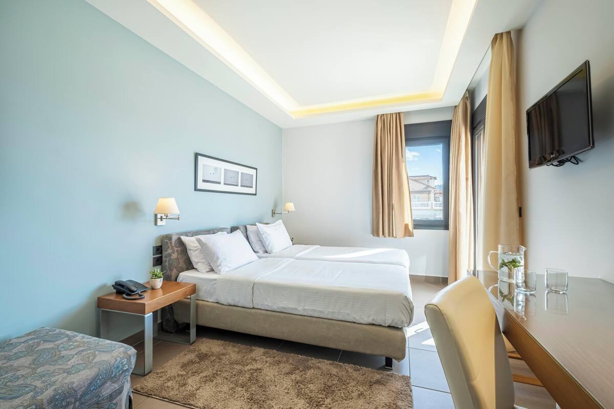 Habitación de hotel con cama, mesita de noche, lámpara, televisión y vista al exterior.