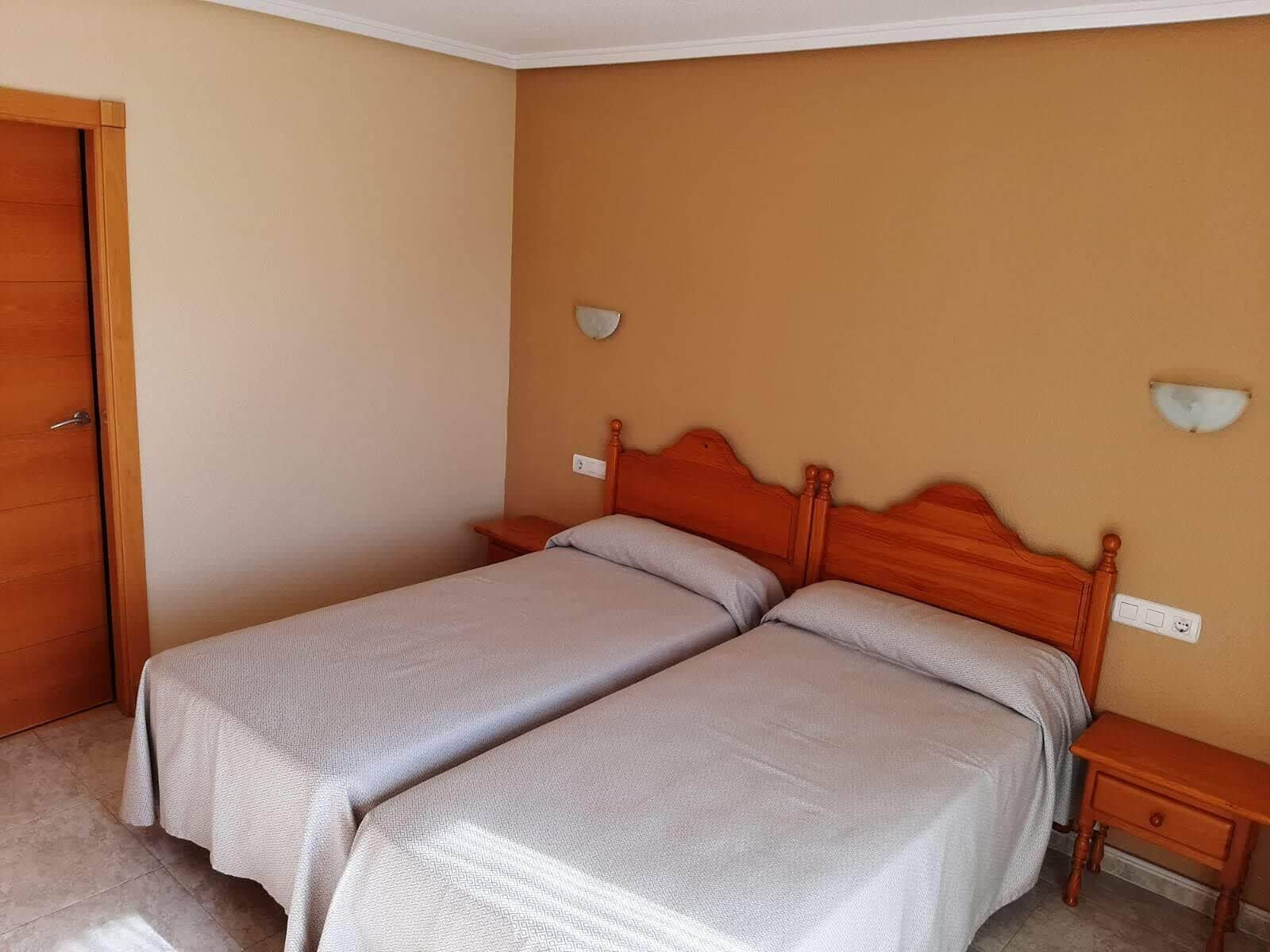 A bedroom with two single beds, wooden headboards, bedside tables, and a door.