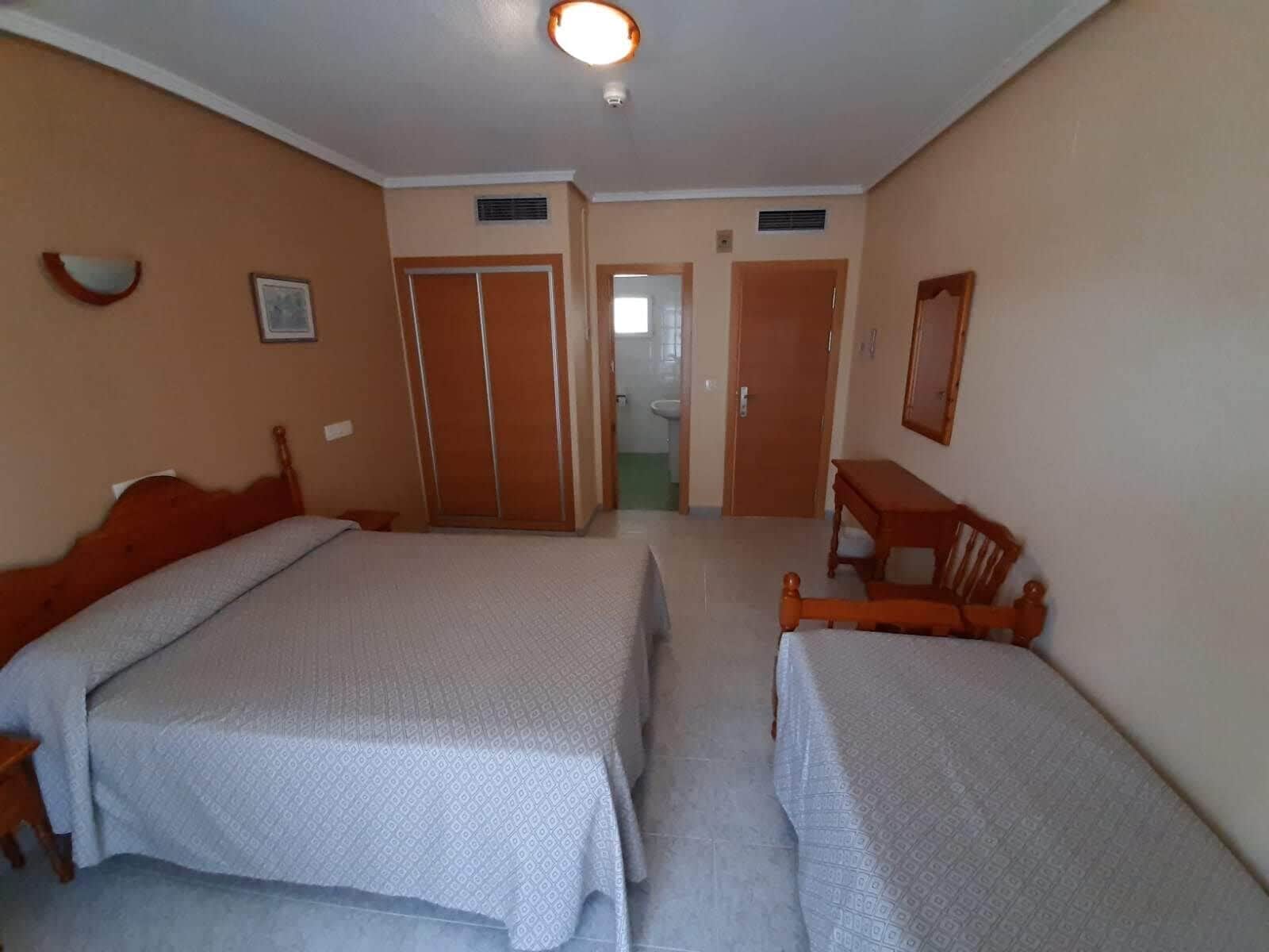 A hotel room with two single beds, a desk, a chair, a mirror, and a door leading to a bathroom.