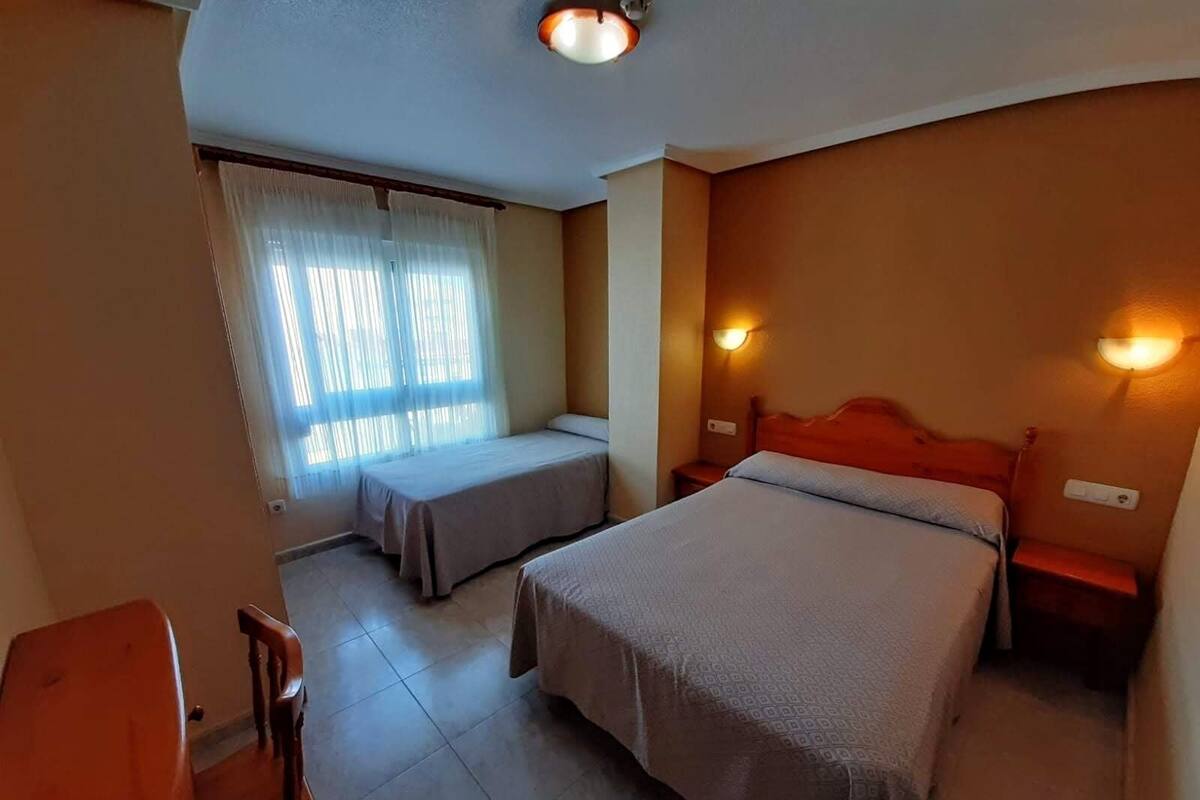 Habitación de hotel con dos camas, un banco, un escritorio y una silla.