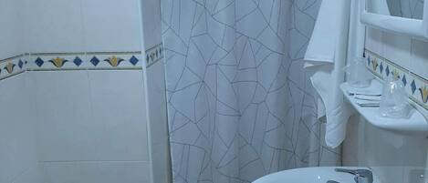 A bathroom with a bidet, a sink, a mirror, and a shower curtain.