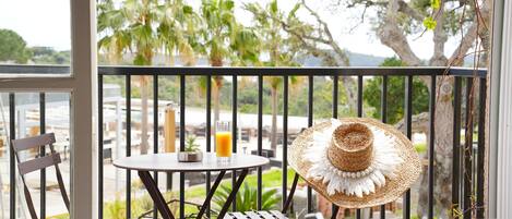 A balcony with a table, chairs, a glass of orange juice, and a straw hat.