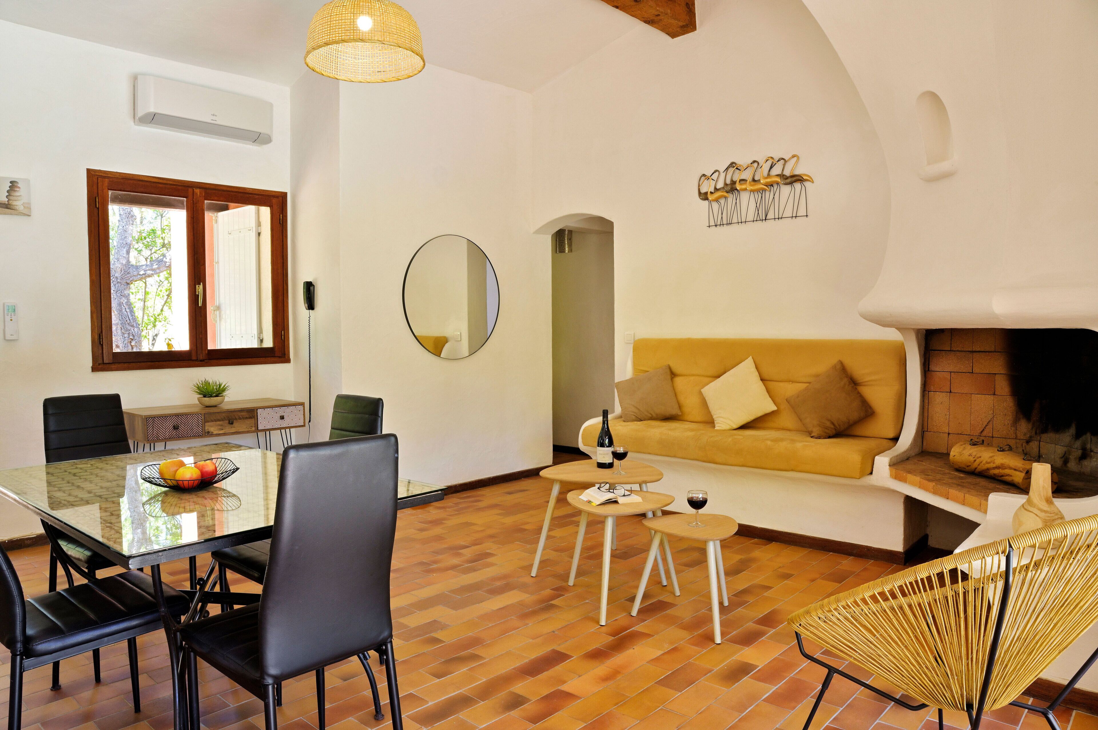Ein Wohnzimmer mit Esstisch aus Glas, schwarzen Stühlen, einem gelben Sofa, einem Kamin und einer Pendelleuchte.