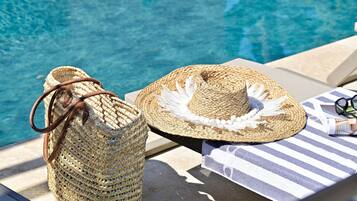 Un bolso de mimbre y un sombrero de paja sobre una tumbona junto a una piscina.