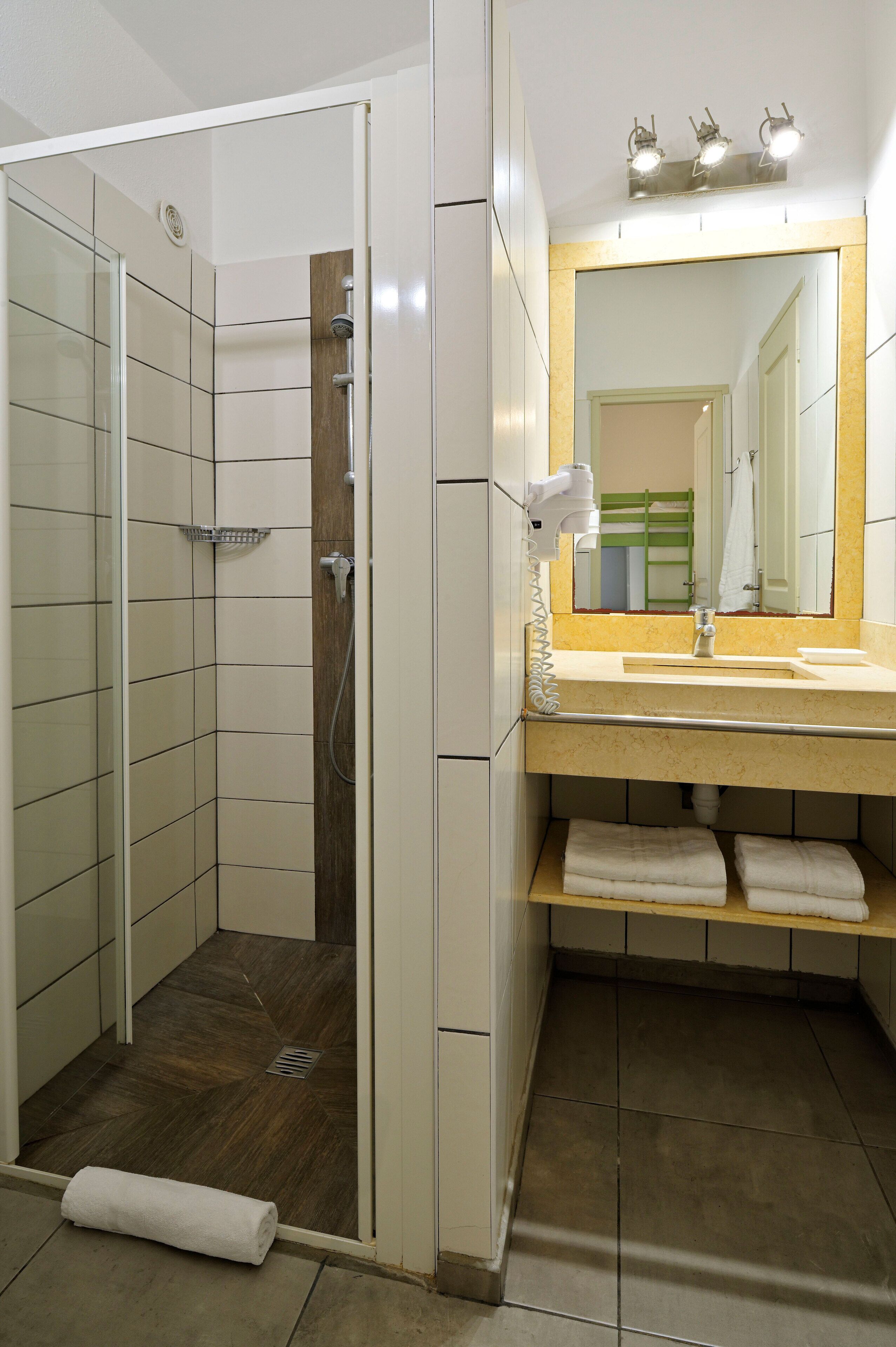 Une salle de bain avec une douche à l’italienne, un lavabo avec un miroir et un porte-serviettes.