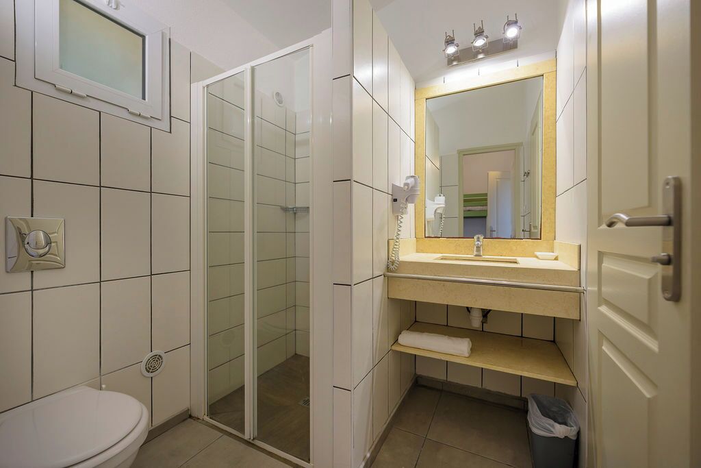 A bathroom with a toilet, a sink with a mirror, and a shower area.
