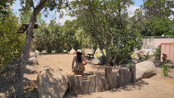 A person walking through a naturalistic setting with trees, rocks, and a wooden fence.