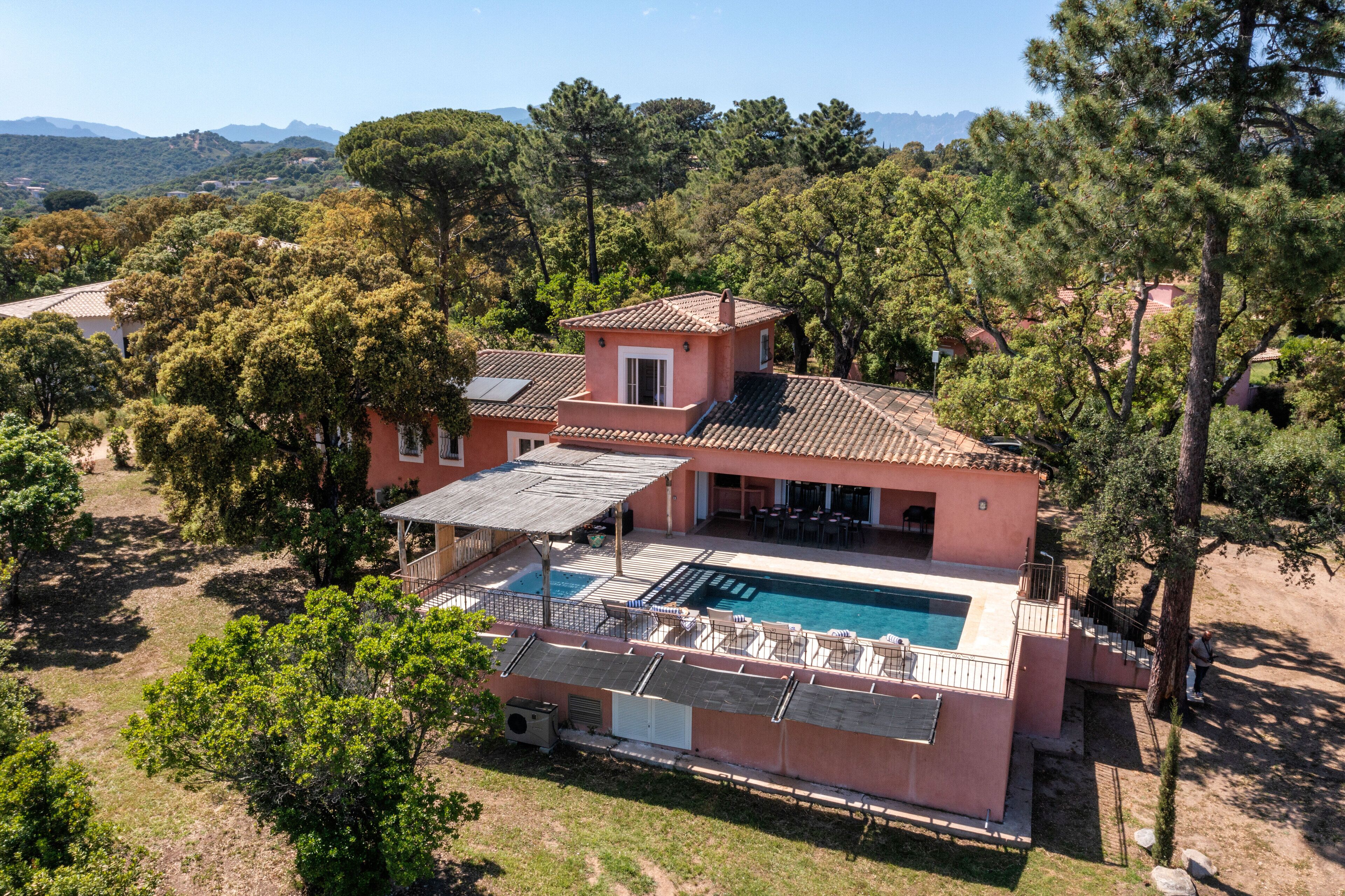 Une villa rose dotée d’une piscine, d’un espace extérieur aménagé et offrant une vue sur la forêt et les collines environnantes.