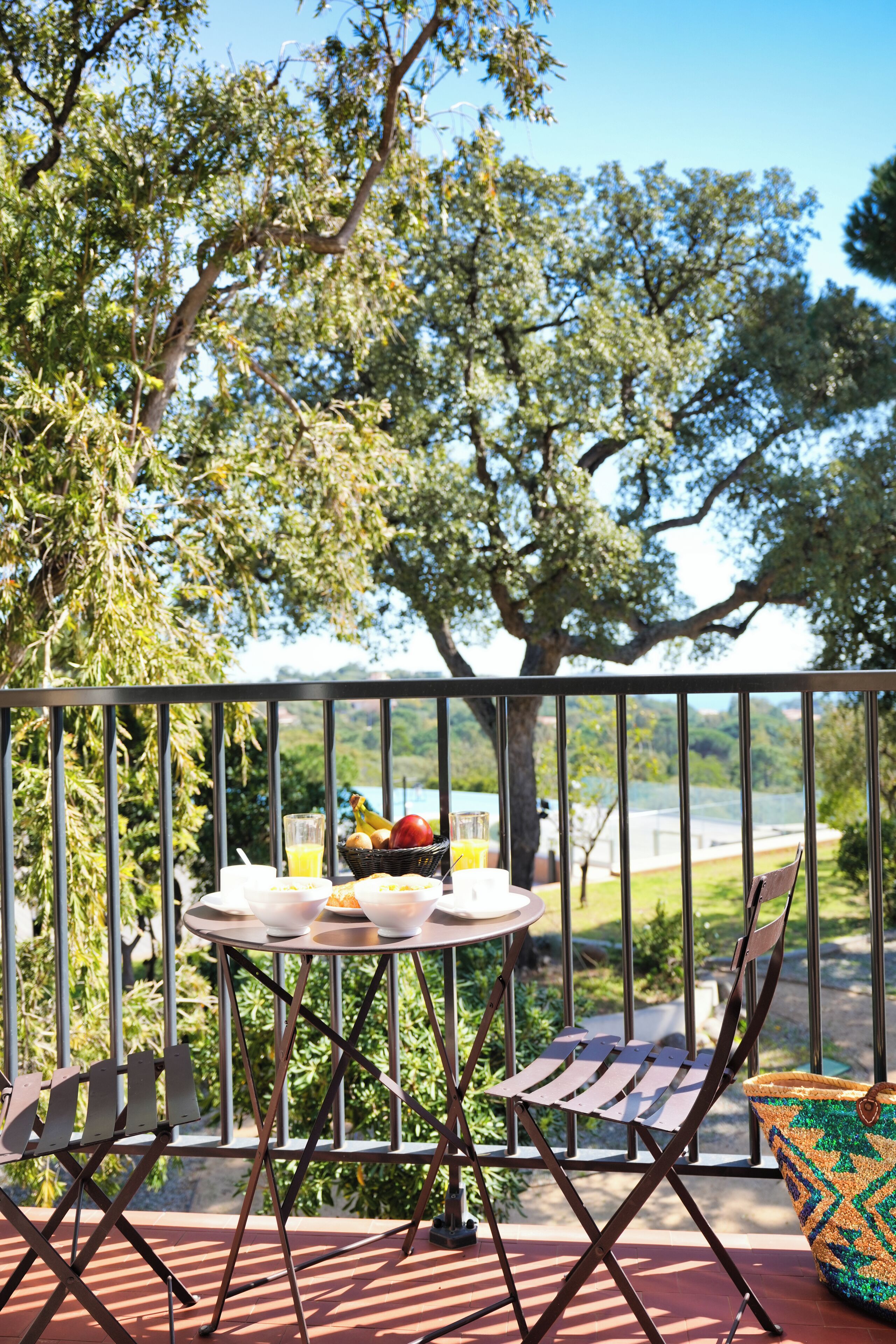 A balcony with a table set for breakfast, a chair, and a view of a lake and trees.