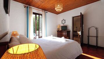 A hotel room with a wooden ceiling, a bed with white linens, a lamp, a TV, and a mirror.