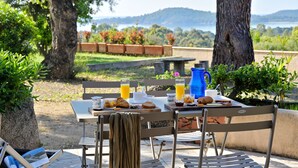 A breakfast setup with a table, chairs, and a view of a lake and hills. - Hotel Residence U Paesolu (Zonza)