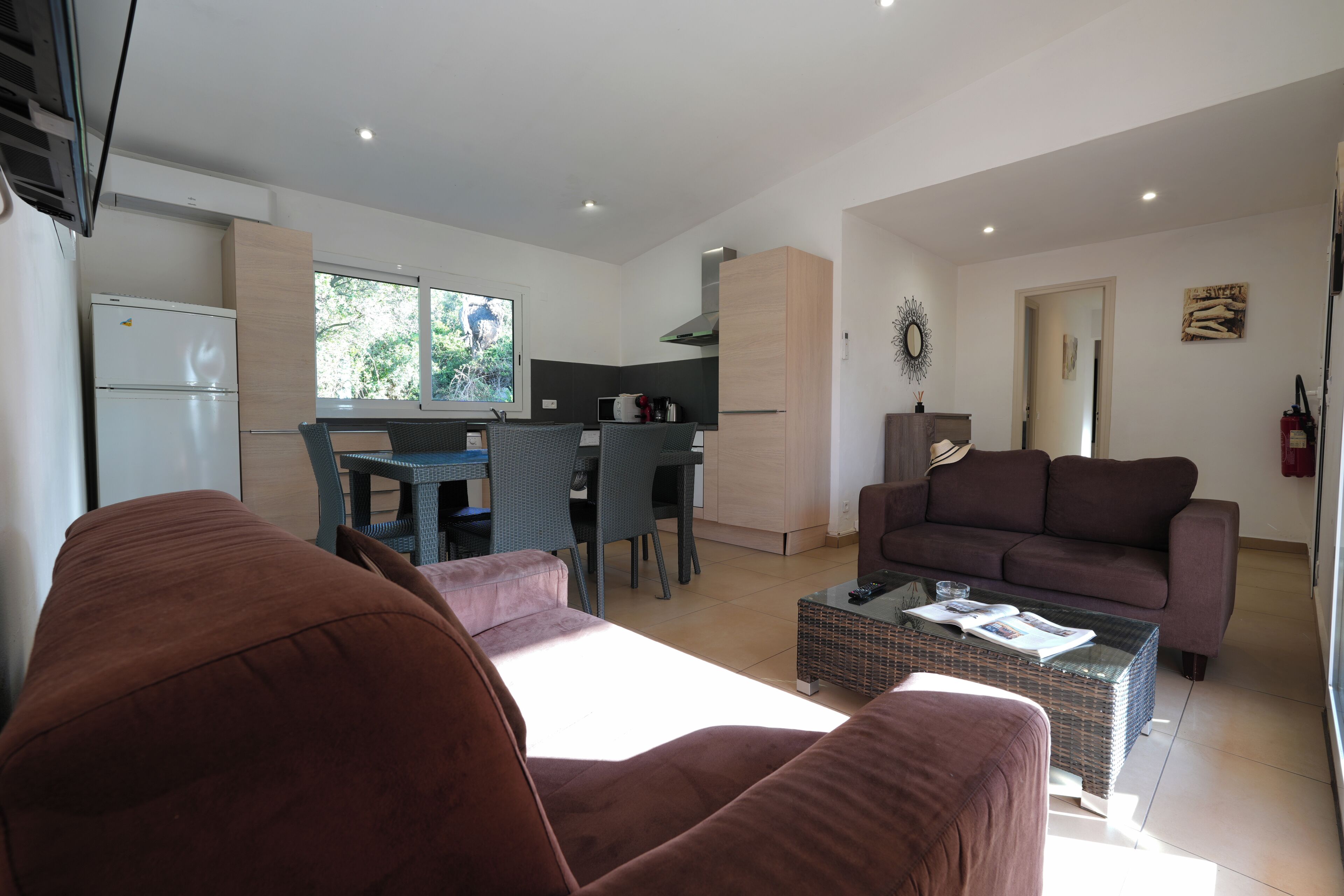 Un salon moderne avec un canapé marron, un coin repas avec une table et des chaises, une cuisine équipée d’un réfrigérateur et d’une fenêtre, et un canapé marron dans l’espace salon.