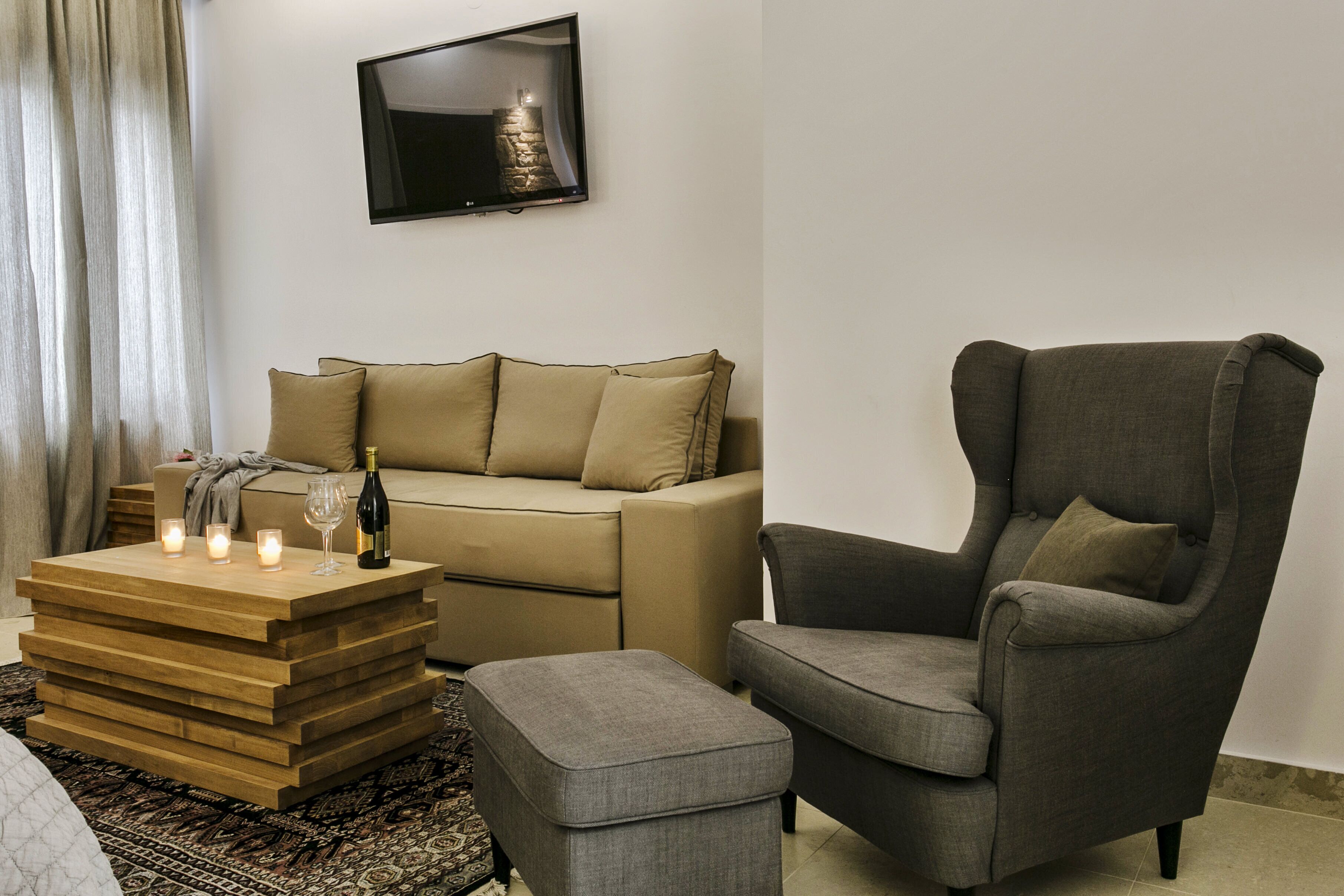 A modern living room with a sofa, a wooden coffee table, a grey armchair, and a flat-screen TV mounted on the wall.