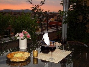 A table set with a dessert, a candle, and wine glasses, overlooking a cityscape at sunset. - Vision Aparthotel (Budapest)