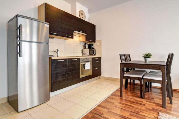 A modern kitchen with a stainless steel refrigerator, dark cabinetry, a microwave, and a dining area with wooden chairs and a table. - Vision Aparthotel (Budapest)