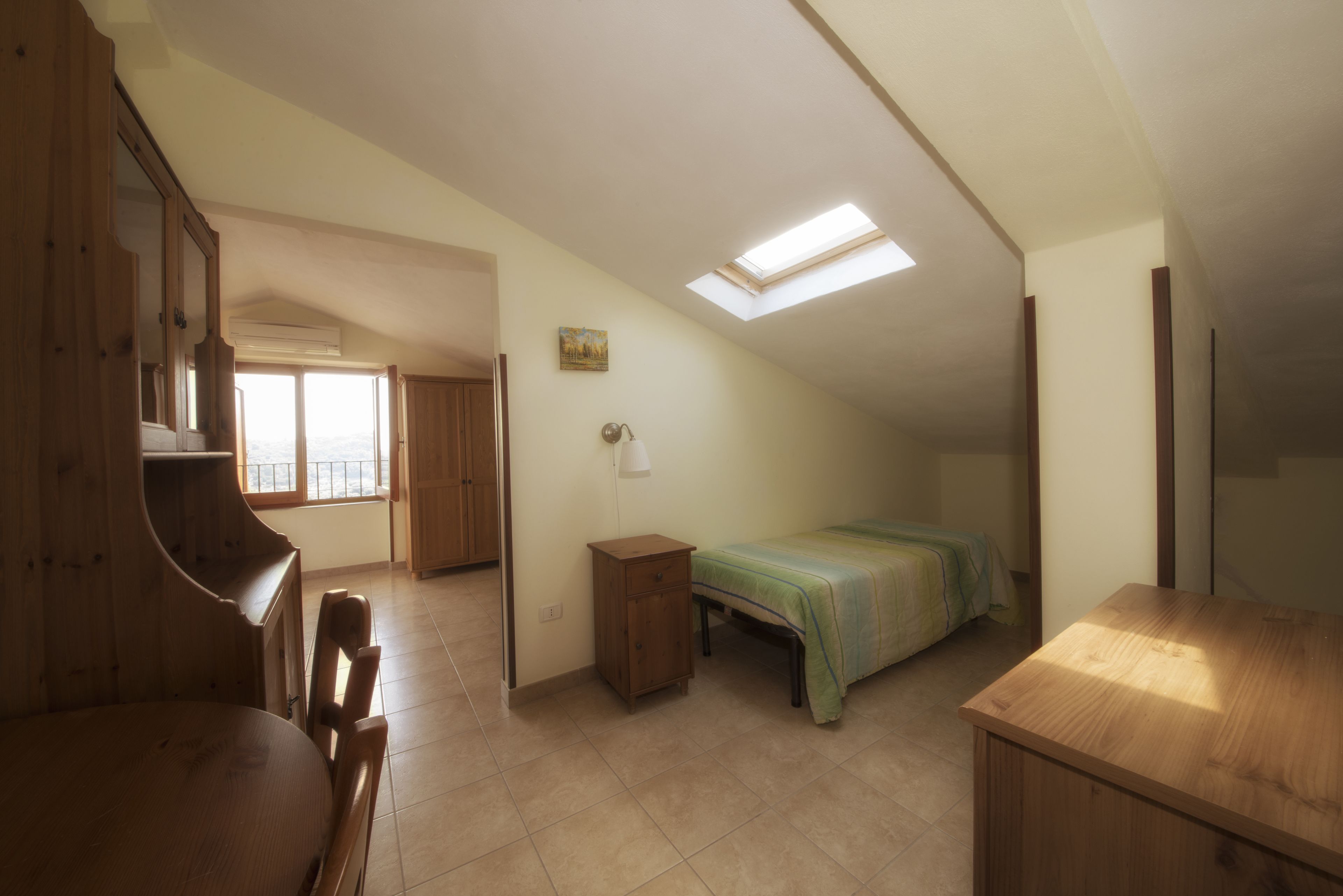 A room with a sloped ceiling, a skylight, a bed, a desk, and a chair.