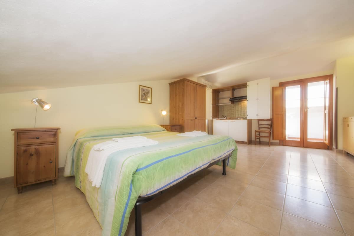 Une chambre avec un lit, une commode en bois et un coin cuisine.