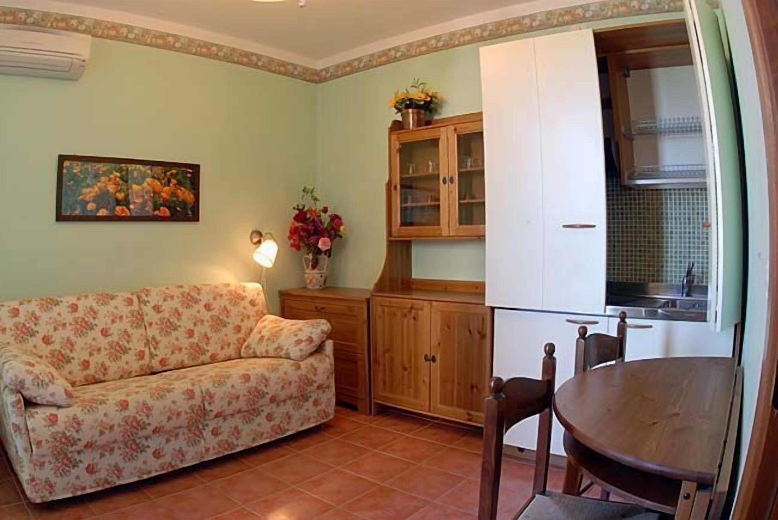 A cozy living room with a floral sofa, wooden cabinets, and a dining table.