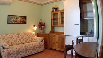 A cozy living room with a floral sofa, wooden cabinets, and a dining table.