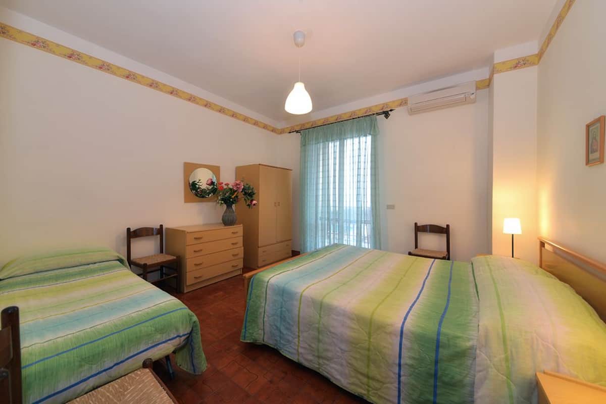Une chambre avec deux lits, une commode, un miroir et une fenêtre avec des rideaux.