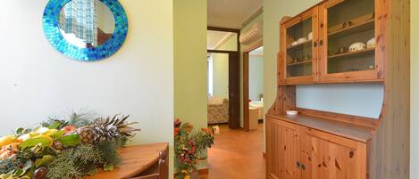 Un couloir avec un meuble en bois, une table à manger agrémentée d’un arrangement de fruits et un miroir en mosaïque accroché au mur.
