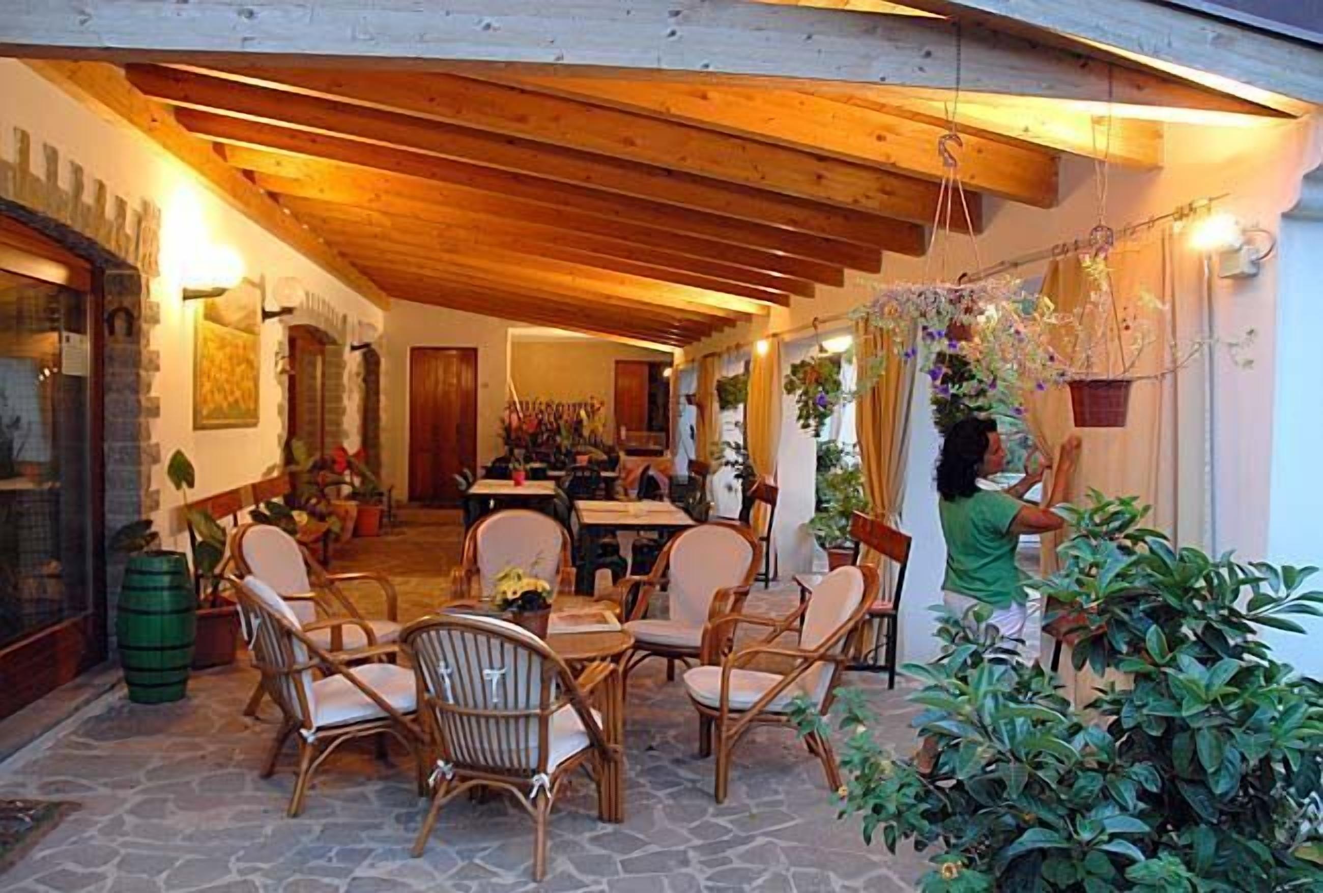 An outdoor dining area with wicker chairs and a stone floor, featuring a wooden ceiling and potted plants.