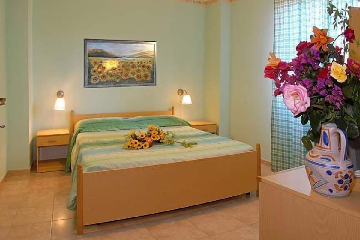 Une chambre à coucher comprenant un lit, deux tables de chevet, une commode, un tableau accroché au mur et un vase avec des fleurs.