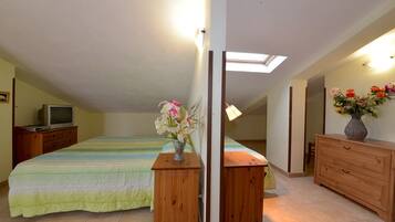 Un dormitorio con una cama, mesitas de noche de madera, un televisor, un florero con flores y un aparador.