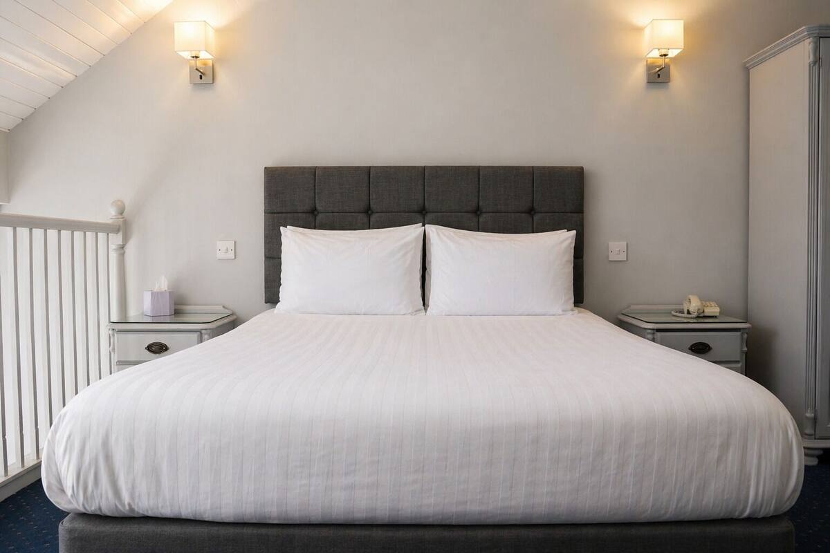 A bed with a grey upholstered headboard, two bedside tables with lamps, and a white bedside table with a telephone.