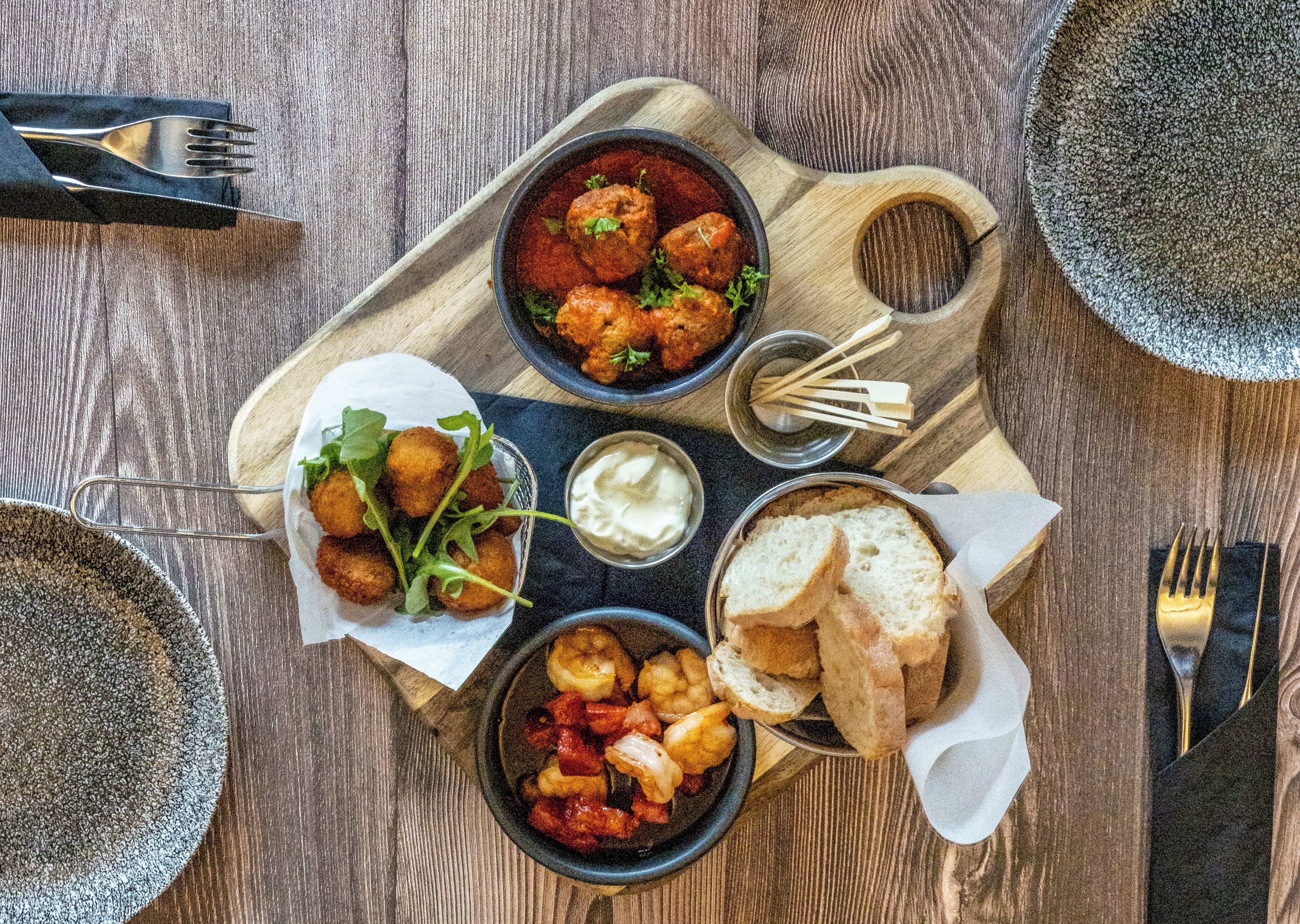 Una tabla de madera con diferentes platos, incluyendo pan, un bol de albóndigas y un bol de verduras.