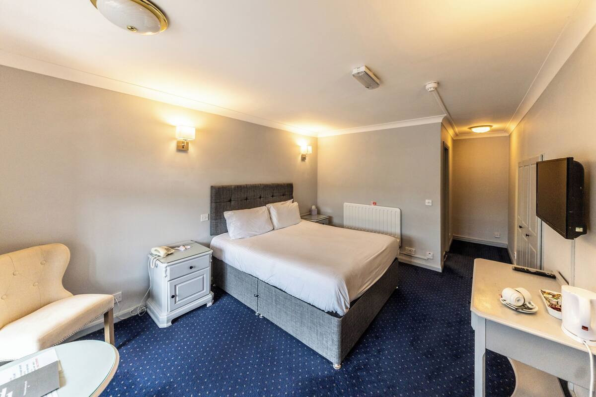 A hotel room with a bed, bedside table, chair, desk, and a television.