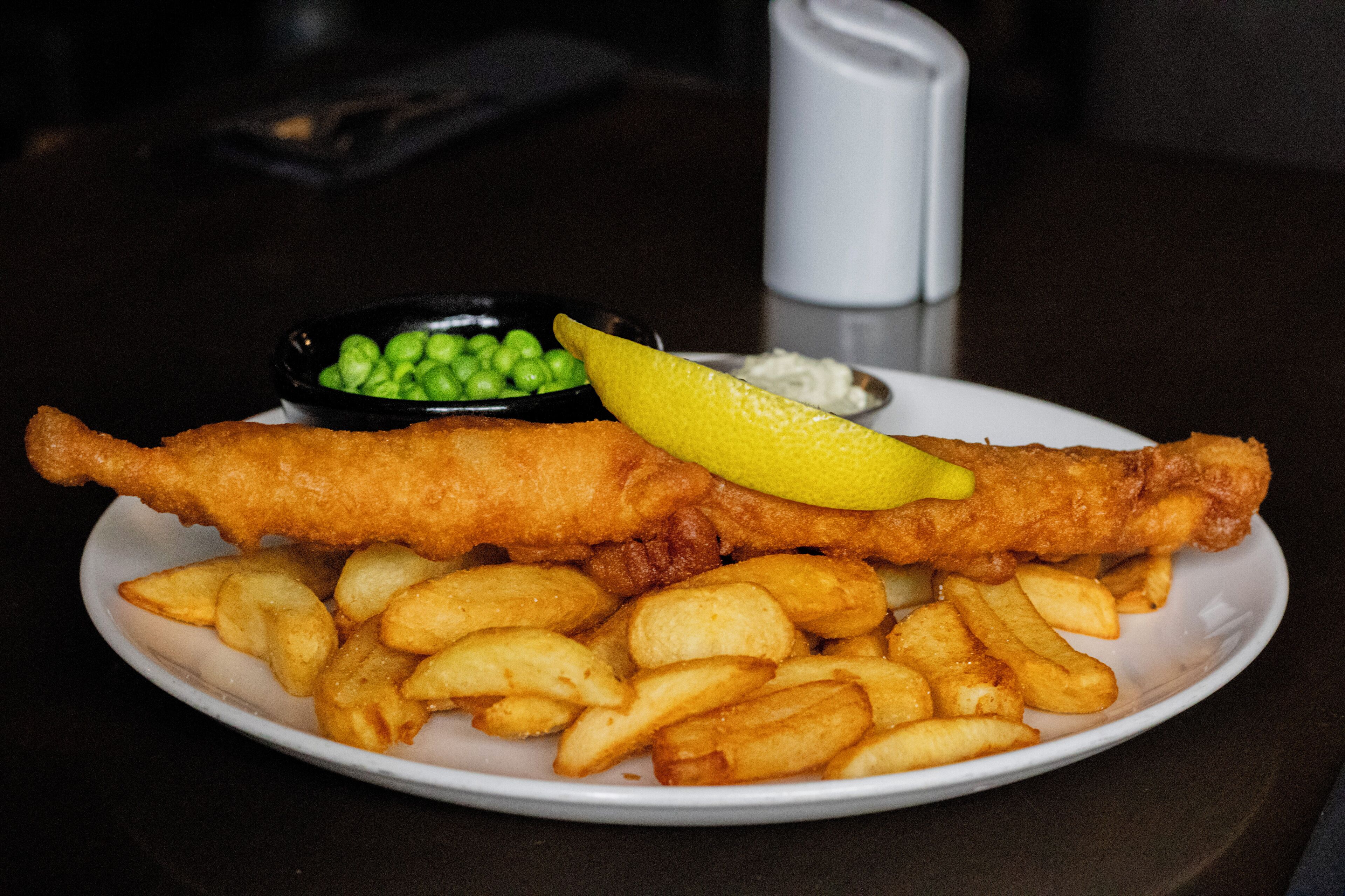 A plate of fish and chips with a lemon wedge and peas.