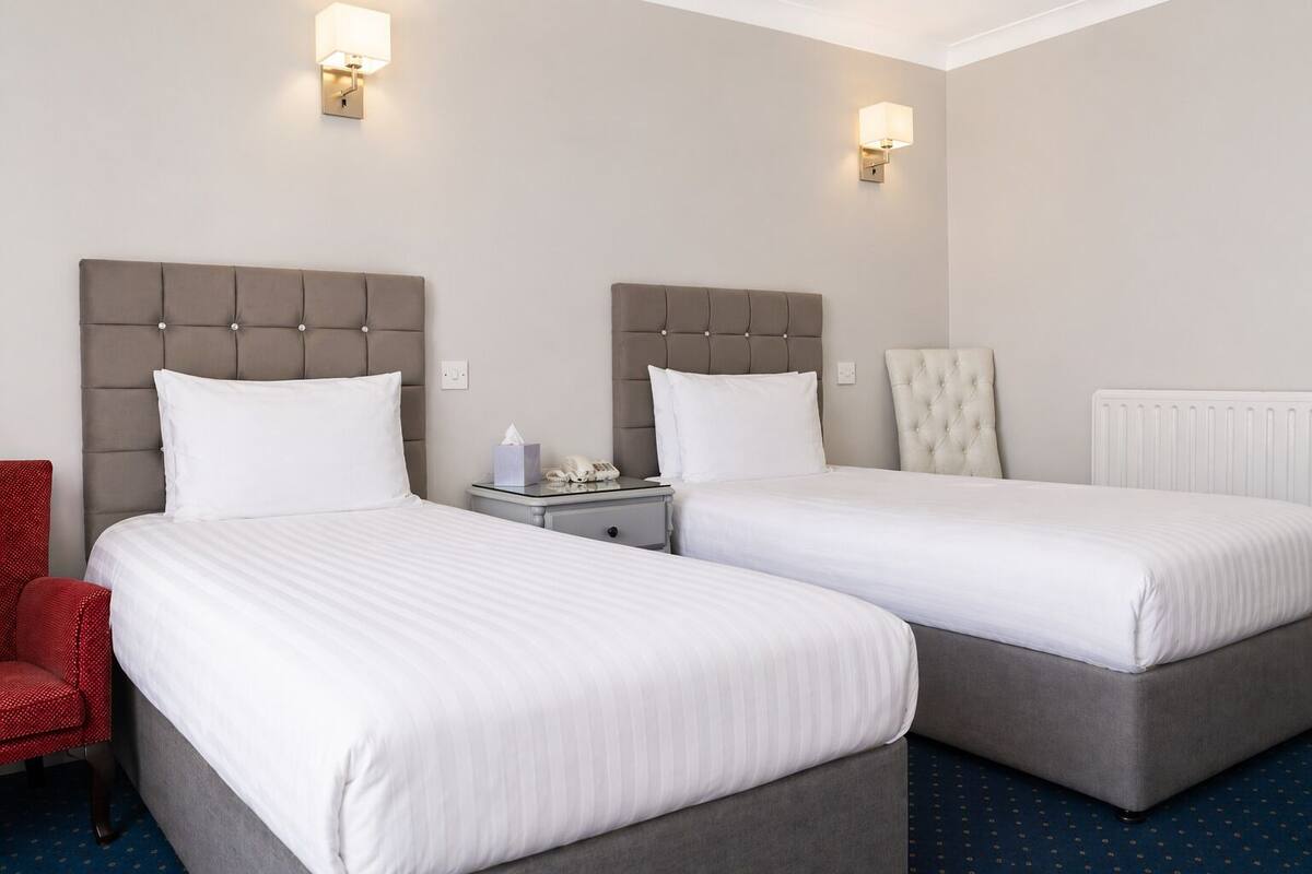 A hotel room with two beds, a red chair, and a nightstand with a lamp and phone.