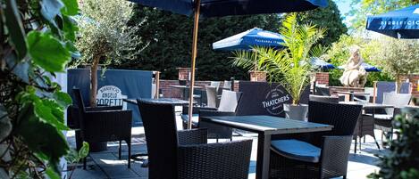 An outdoor patio with wicker chairs and tables, blue umbrellas, and a statue.