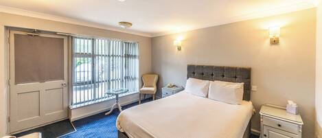 Une chambre d’hôtel avec un grand lit, une table de chevet, une chaise, un bureau et une fenêtre avec des stores.