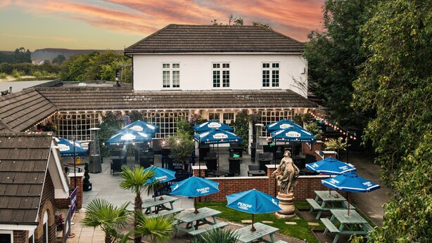 A courtyard with outdoor seating, a statue, and a white building in the background. - The Littleover Lodge Hotel (Derby)