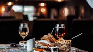 Una mesa de comedor con una hamburguesa, papas fritas y dos vasos de vino.