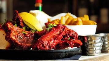 Une assiette d’ailes de poulet rouges et laquées, accompagnées de quartiers de citron et d’une portion de frites dorées.